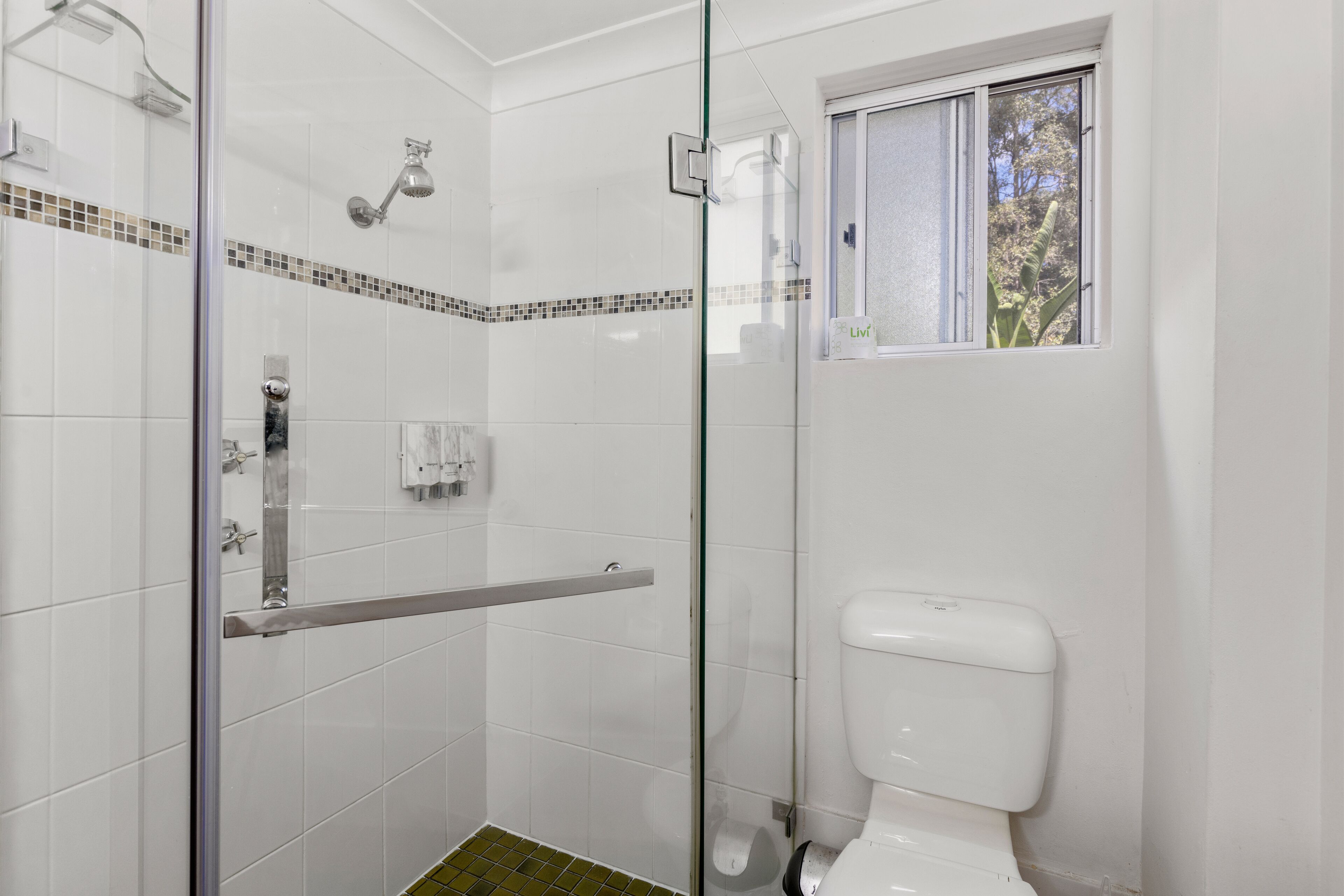 A modern bathroom with a glass-enclosed shower, a toilet, and a window providing natural light.