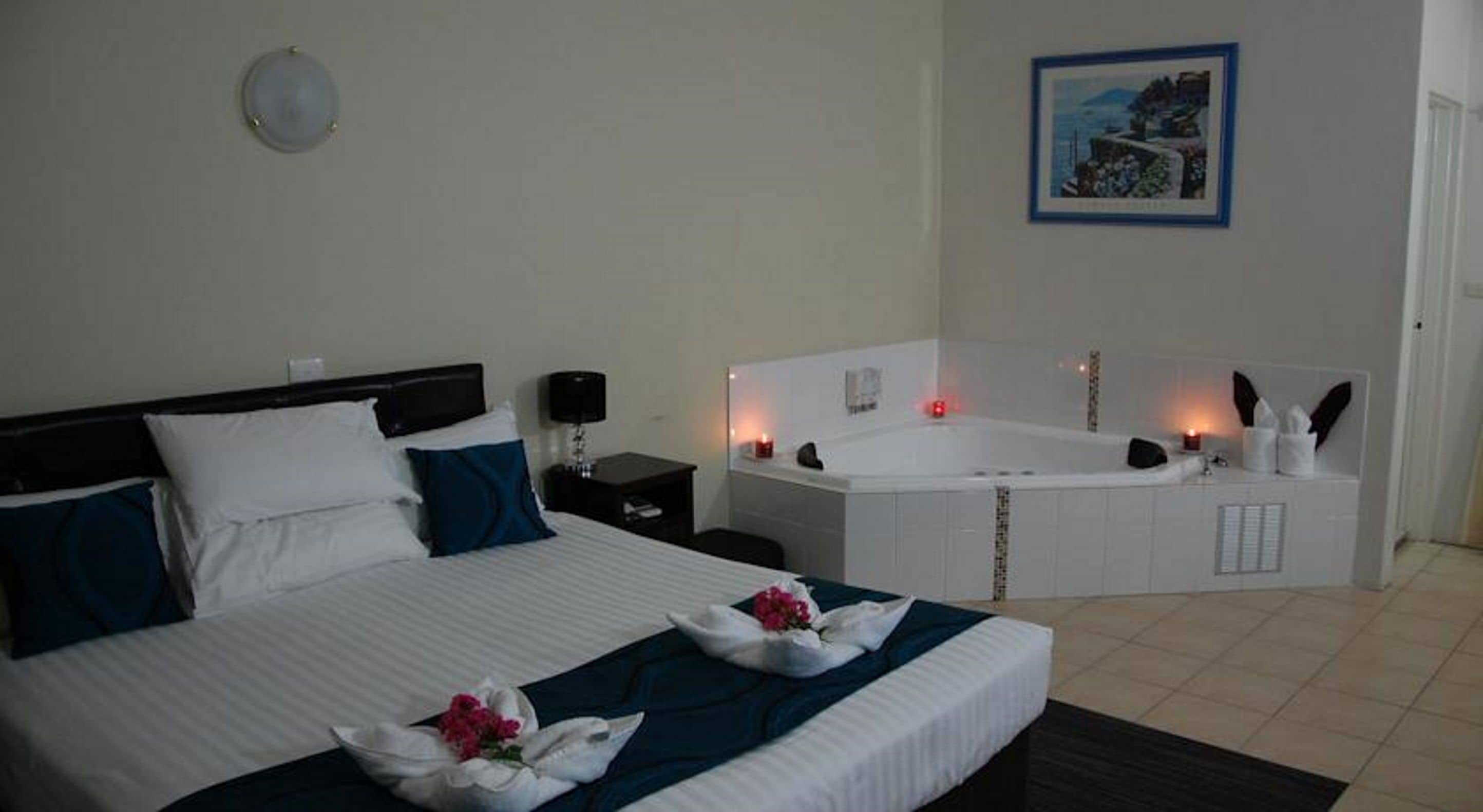 A hotel room with a bed, a nightstand, a desk, a large bathtub, and a framed picture on the wall.