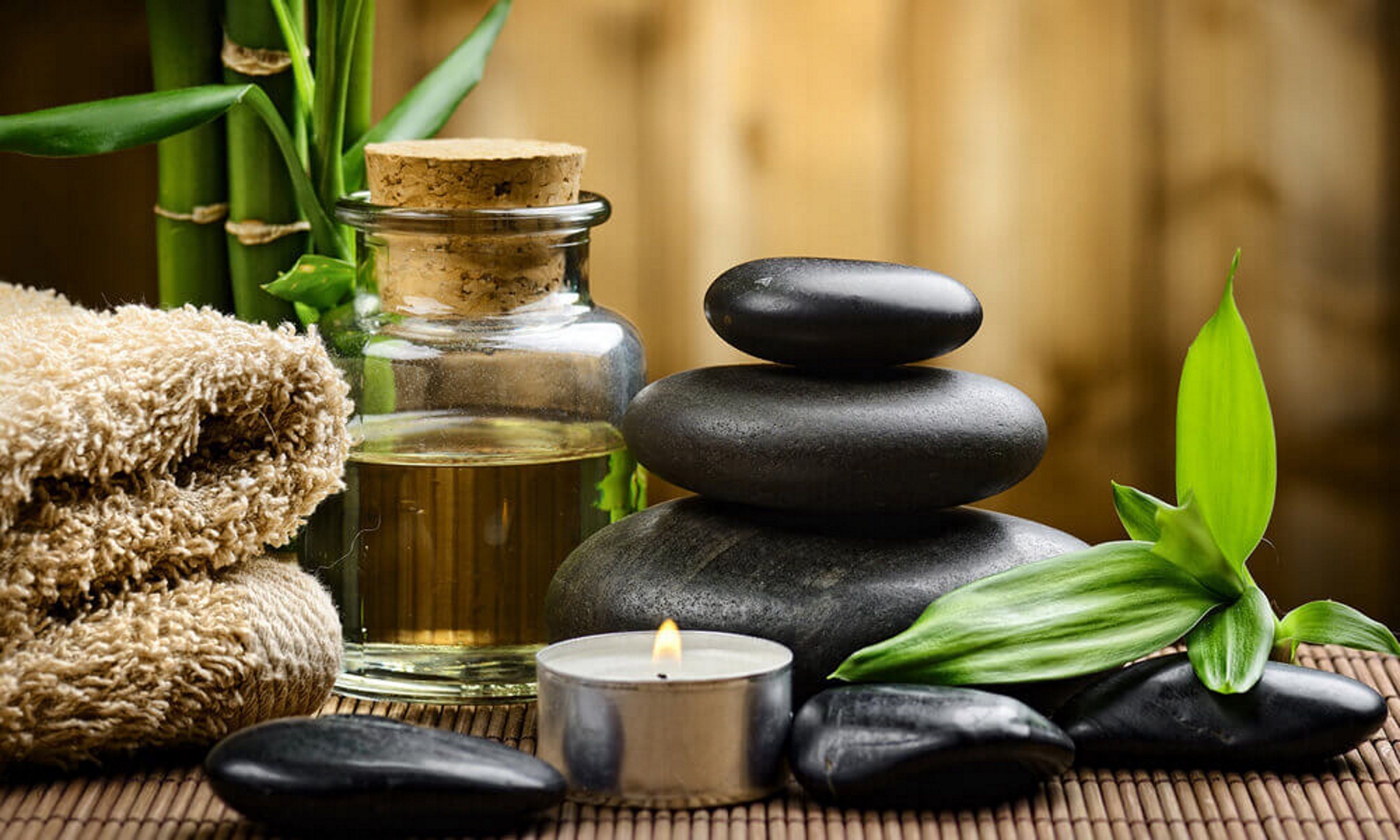 A spa setting with a candle, stones, a bottle, and green leaves.