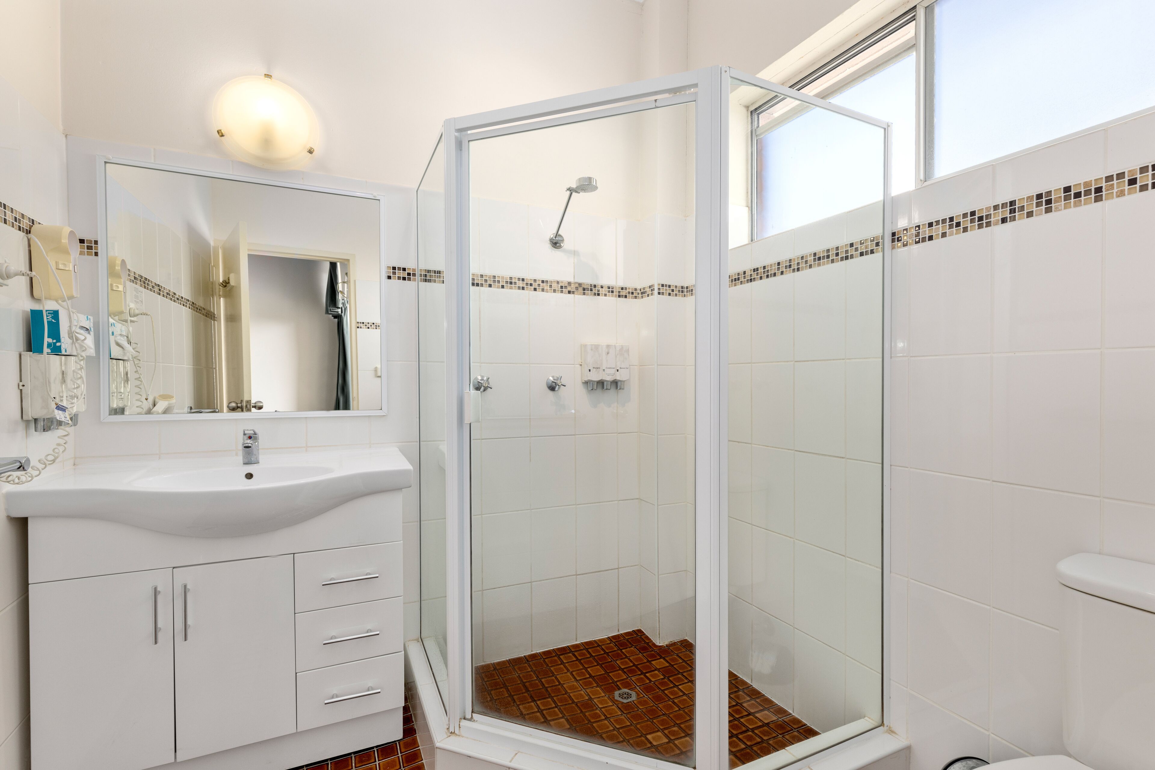 Een badkamer met een douchecabine van glas, een witte wastafel en een betegelde vloer.