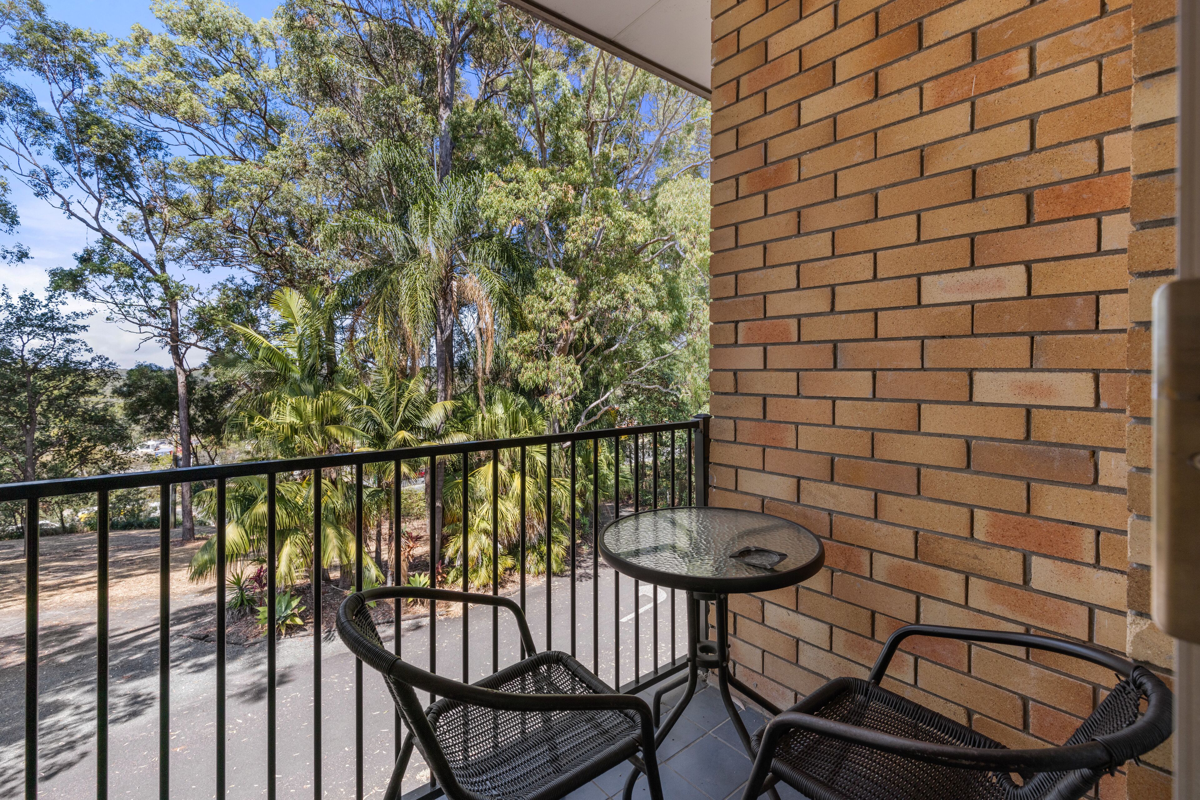A balcony with a brick wall, two wicker chairs, and a small round table.