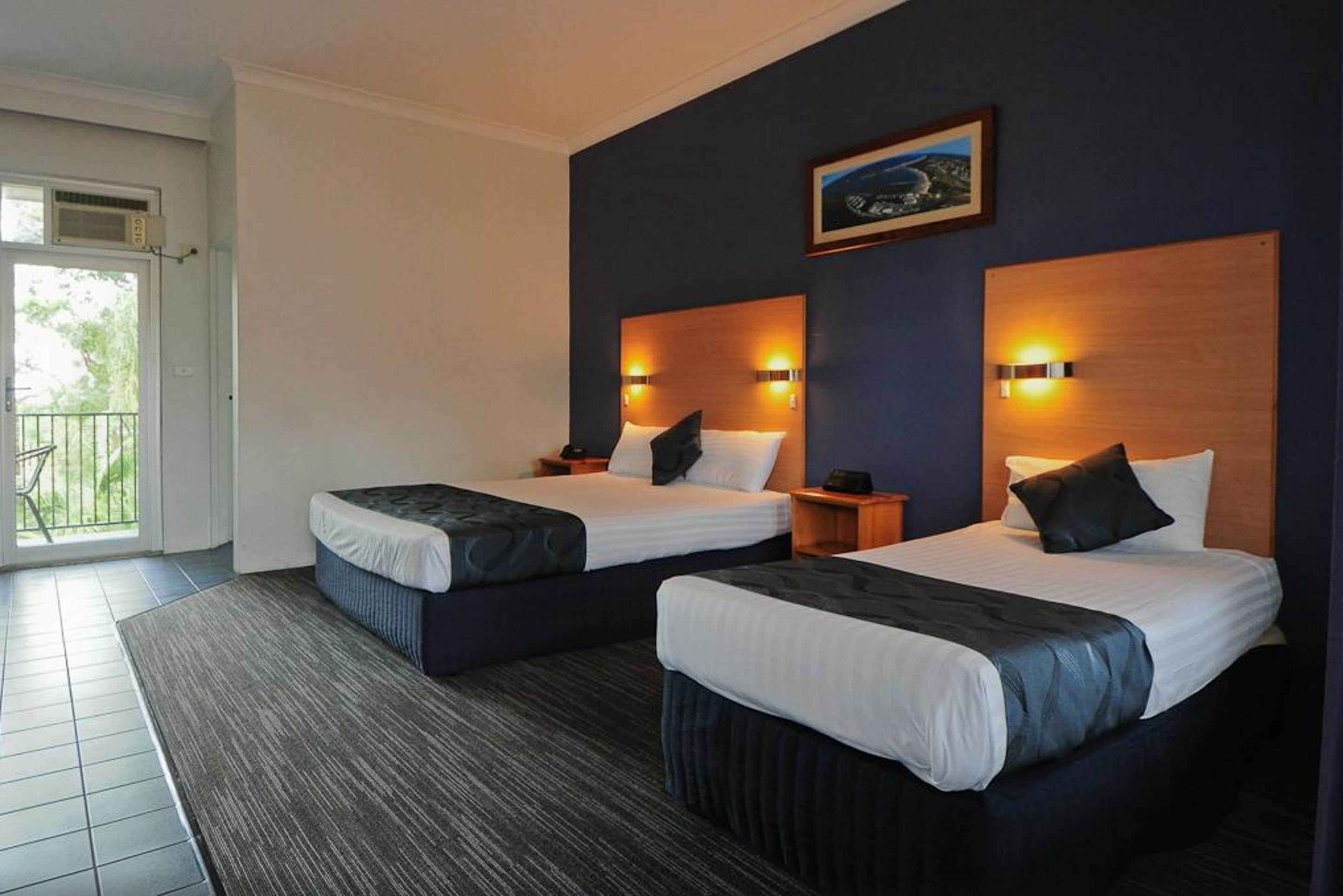 A hotel room with two beds, a large window, and a view of the outdoors.