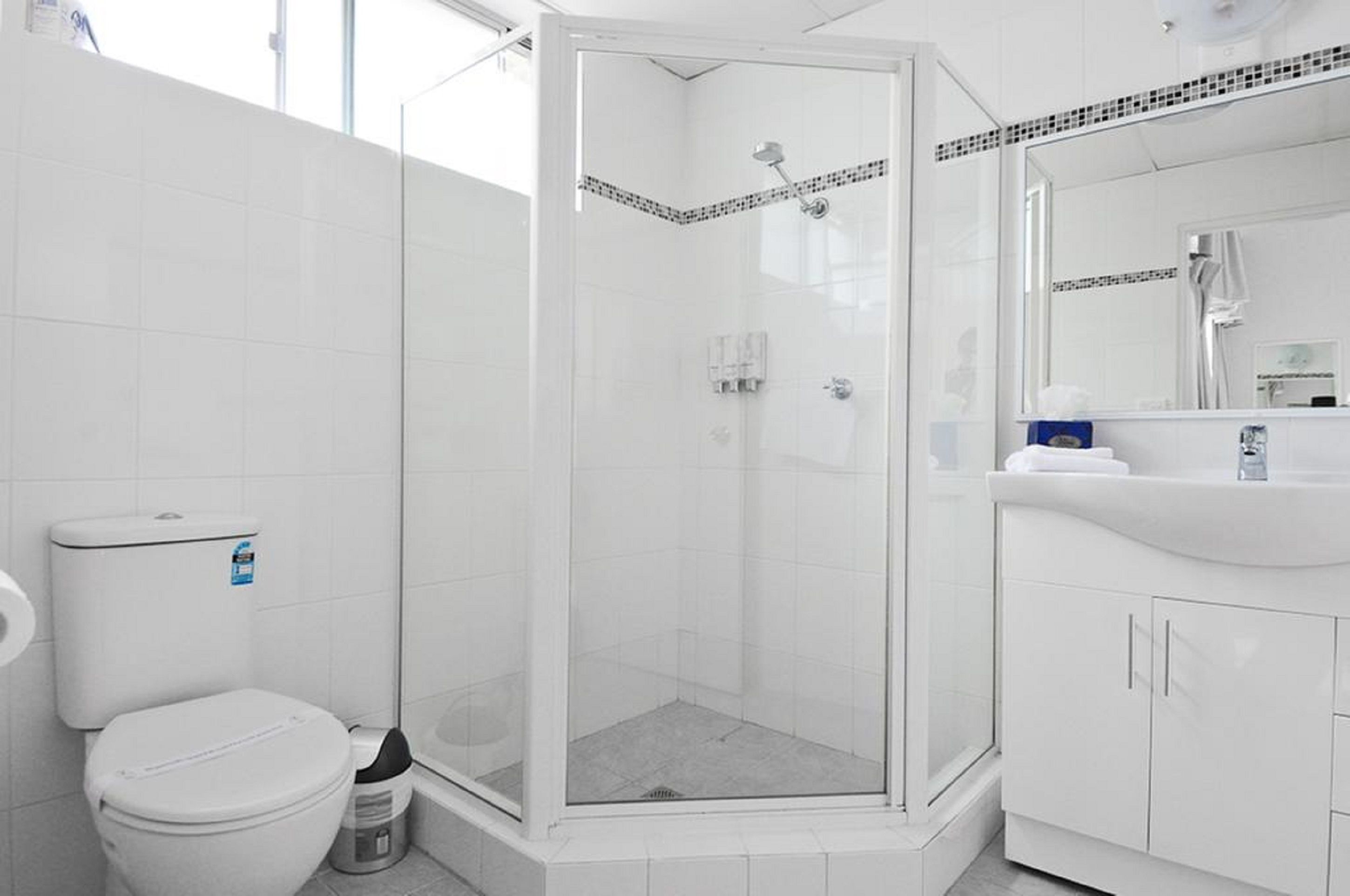 A modern bathroom with a glass-enclosed shower, white tiles, a toilet, and a sink with a mirror.