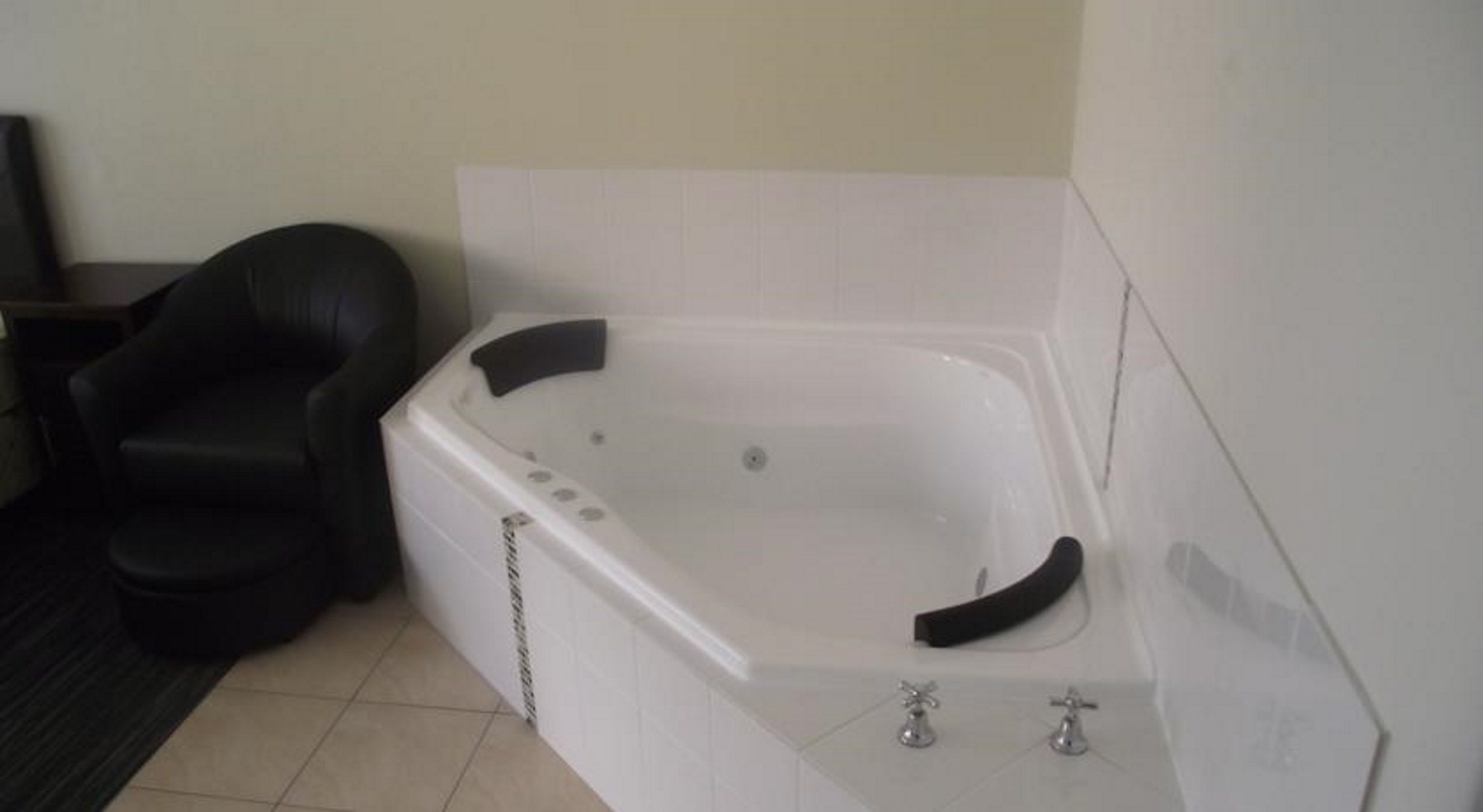 A white bathtub with a black chair beside it, a tiled floor, and a white wall.