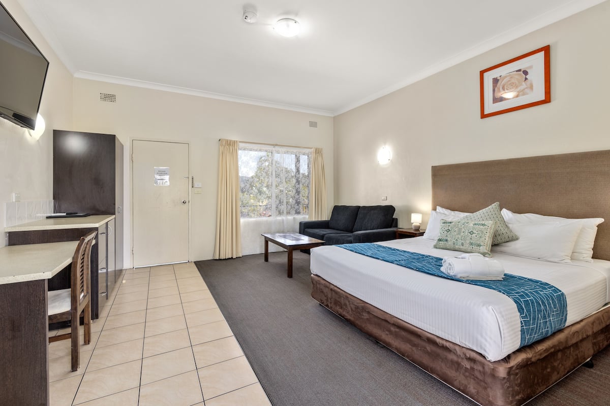 A hotel room with a bed, a desk, a chair, a sofa, and a television.