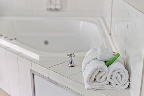 A bathroom with a white bathtub, a towel rack with folded towels, and a green bottle on the counter.
