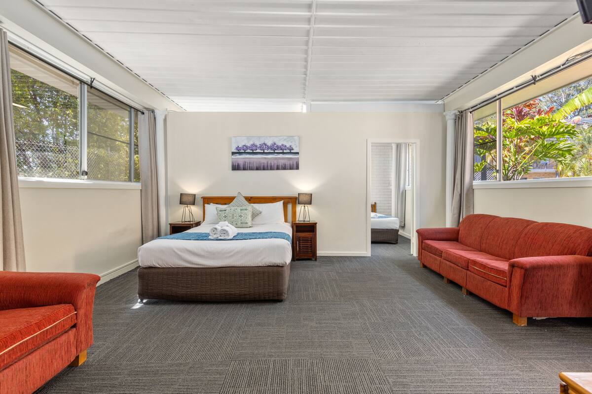 A hotel room with a large bed, a red sofa, a small table, and a painting on the wall.