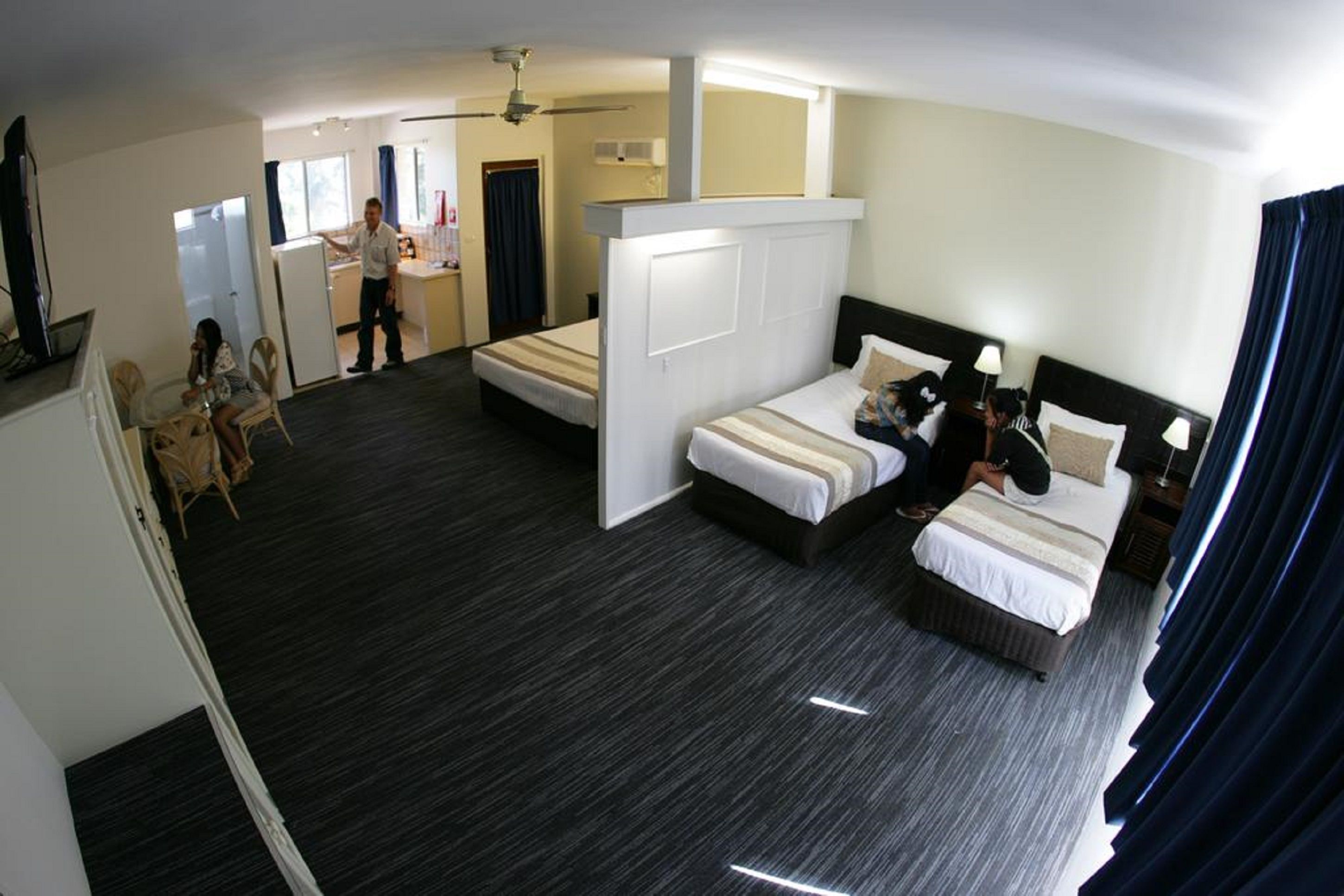 A hotel room with two beds, a kitchenette, a dining area, and a bathroom.
