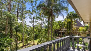 A balcony with a view of a lush garden and a distant building.