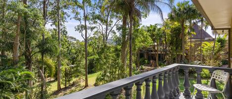 A balcony with a view of a lush garden and a distant building.