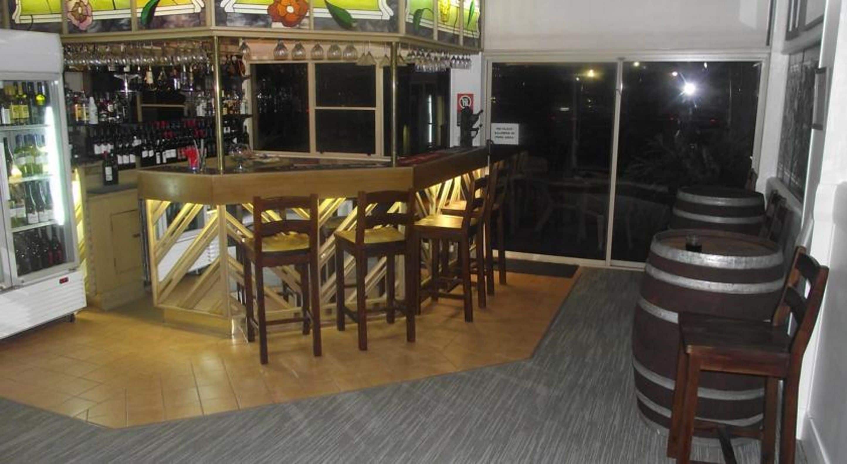 A bar area with wooden chairs, a bar counter, and a refrigerator stocked with bottles.