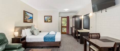 A hotel room with a bed, a green sofa, a wooden table, a TV, and a painting on the wall.