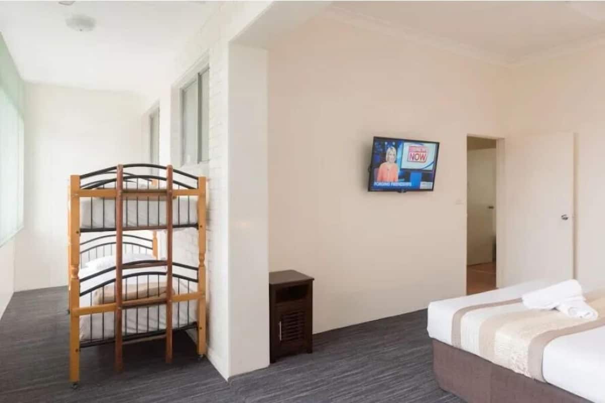 A hotel room with a bunk bed, a television mounted on the wall, and a small bedside table.