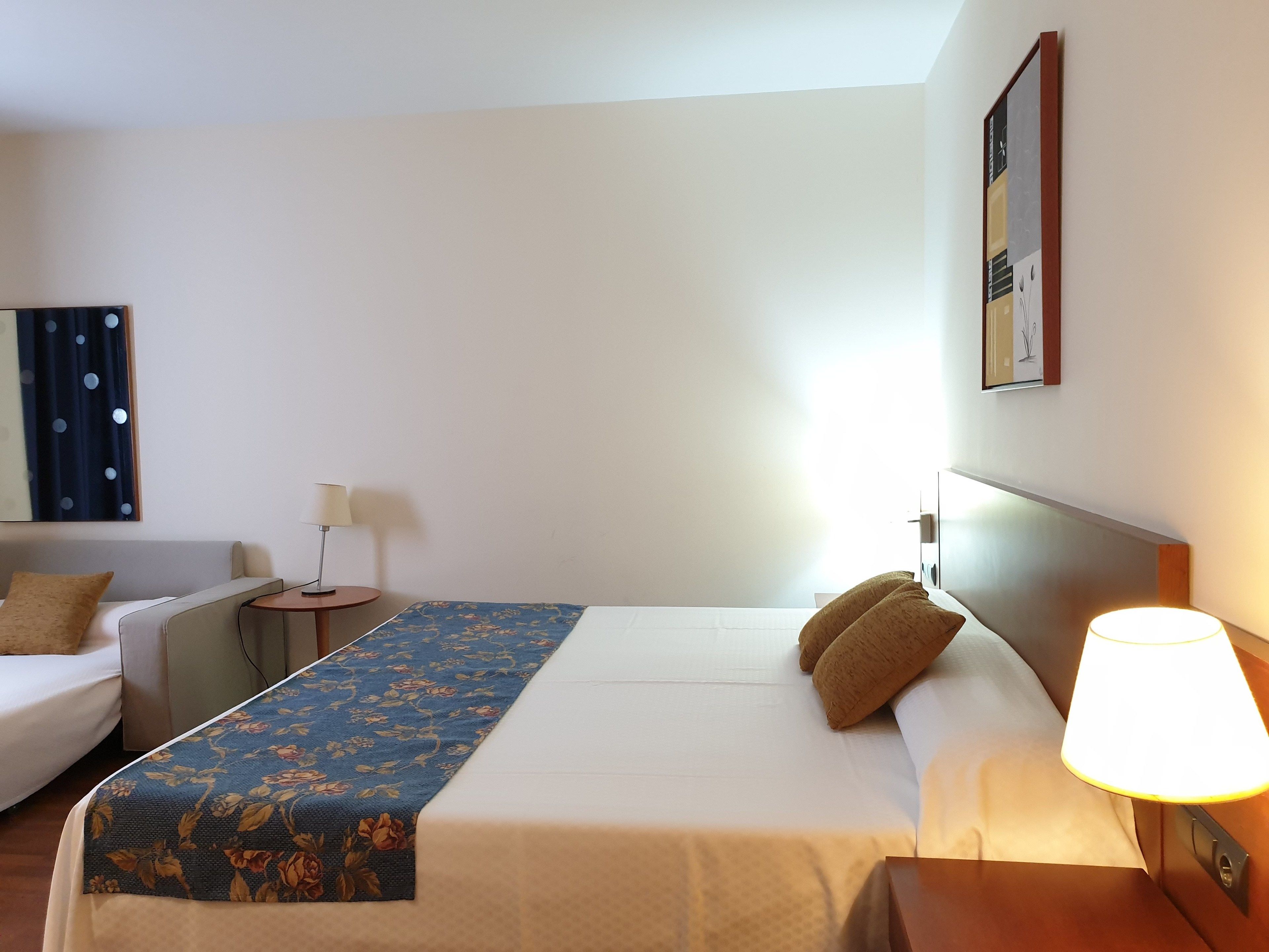 A hotel room with a bed, a sofa, a small table, and a lamp.