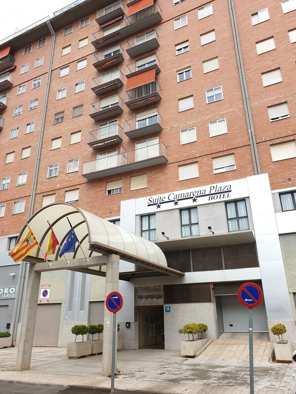 A multi-story hotel with balconies, a covered entrance, and flags.