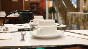 A dining table set with white cups and saucers, cutlery, and a napkin. - Hotel Suite Camarena (Teruel)
