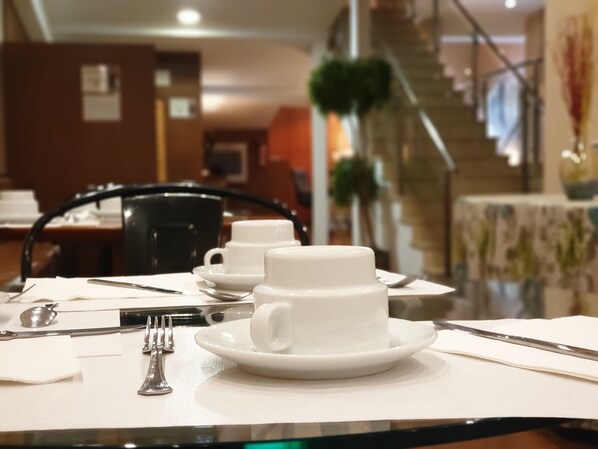 A dining table set with white cups and saucers, cutlery, and a napkin.