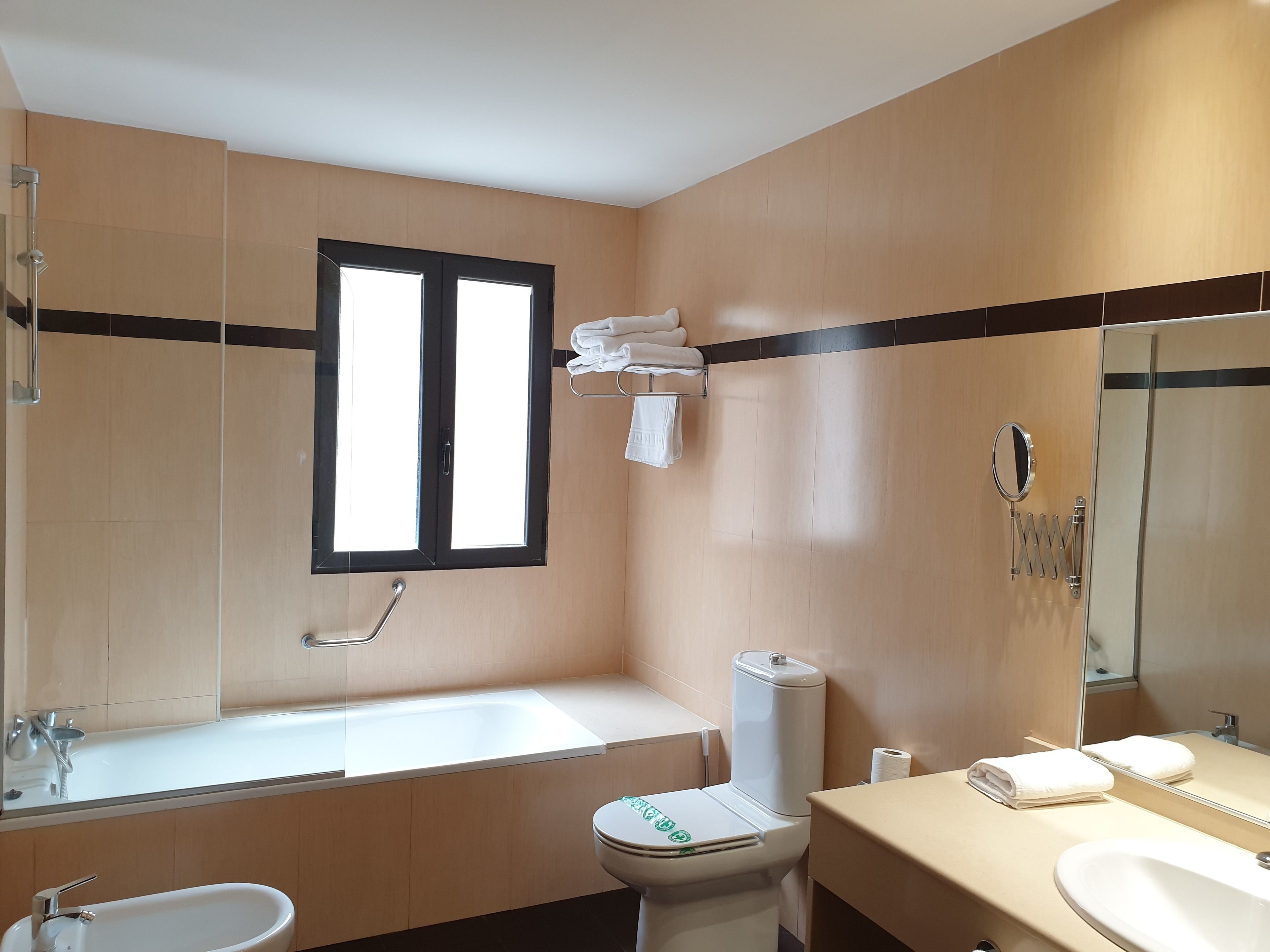 A modern bathroom with a bathtub, toilet, sink, and a window.