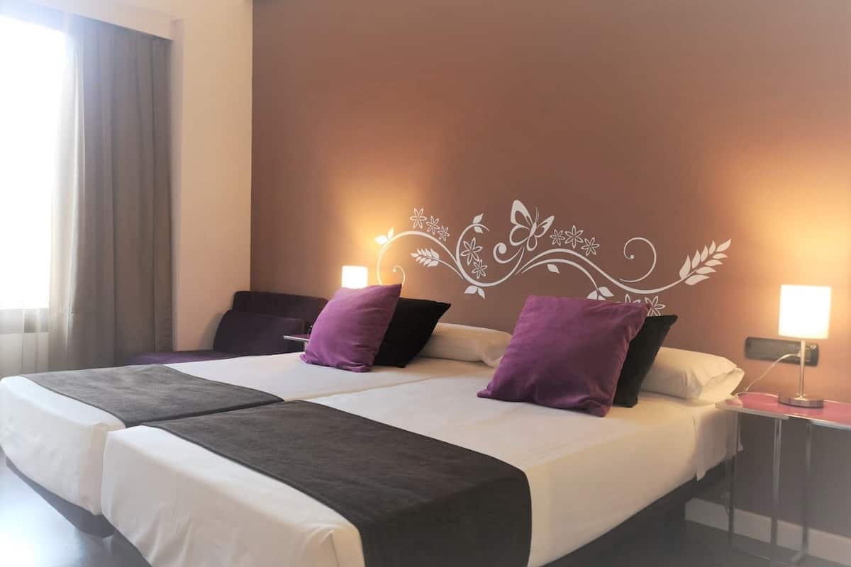 Una cama doble con dos almohadas, una mesita de noche con lámpara y un diseño decorativo en la pared.