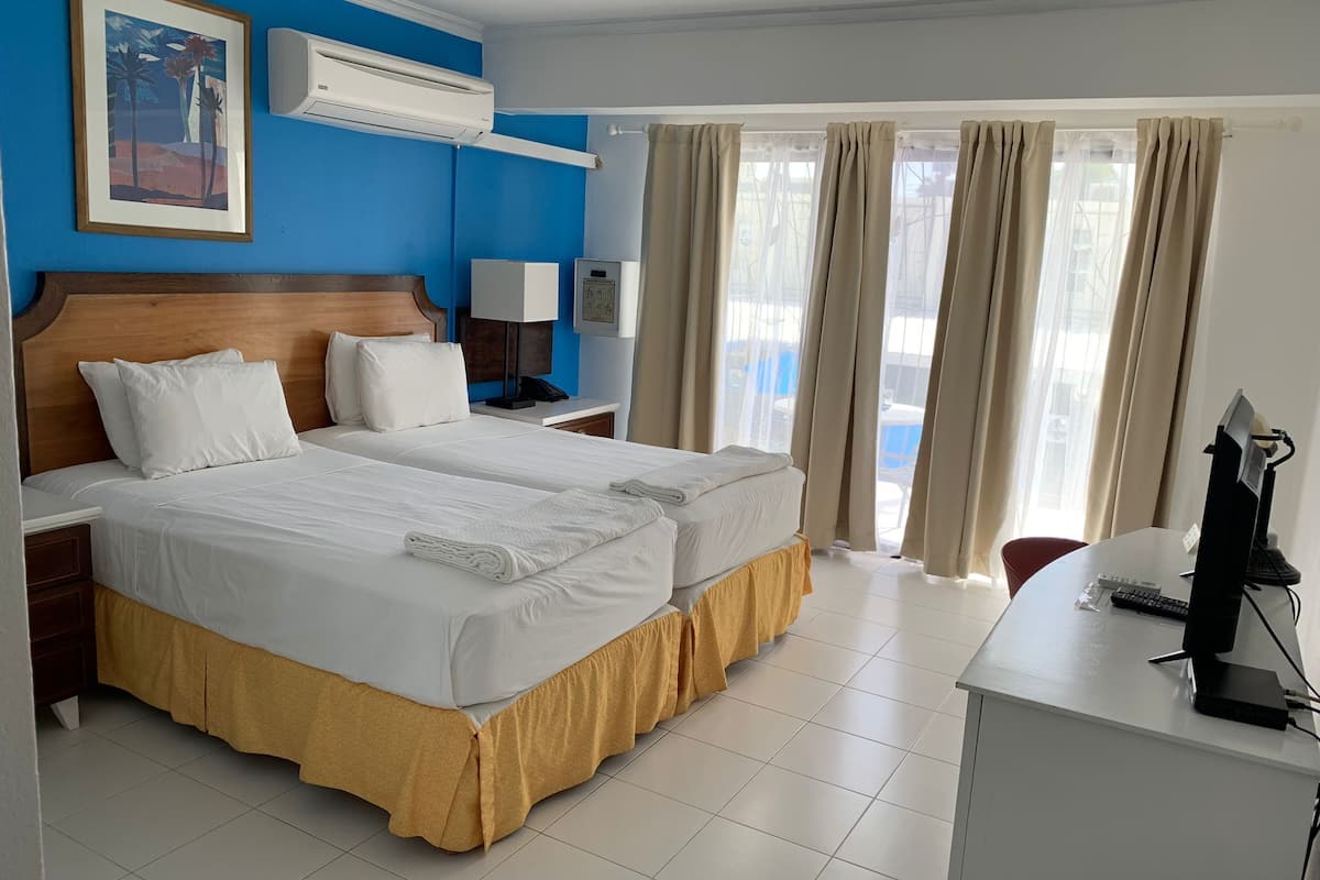 A hotel room with two beds, a desk with a computer, a lamp, and a window with curtains.