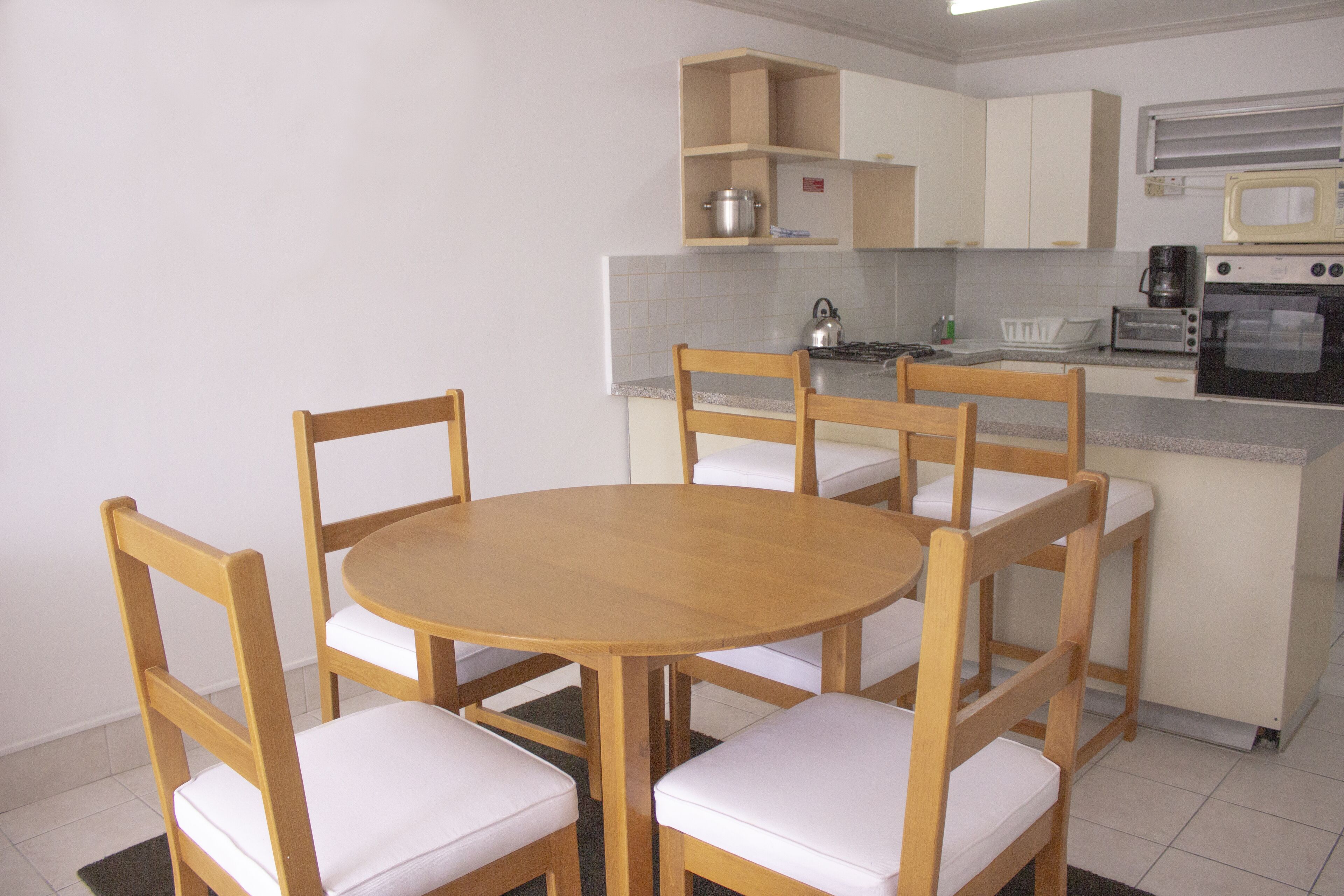 A small kitchen with a round wooden table and four chairs, a microwave, a toaster, and a kettle.