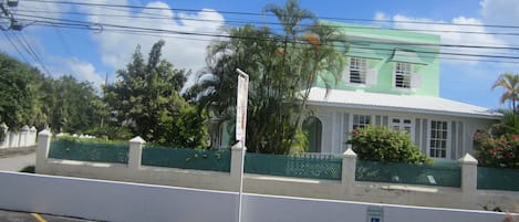 A building with a green roof and white walls, surrounded by a green fence and palm trees.