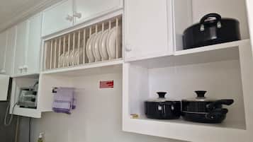 A kitchen with white cabinets, a dish rack, a microwave, and two black pots on the shelves.