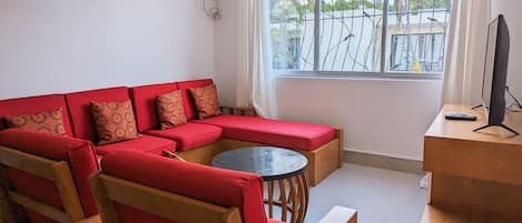 A living room with a red sofa, a round coffee table, and a TV on a wooden stand.