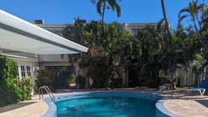 A clear blue pool with a 3.5 ft depth marker, surrounded by palm trees and a covered area.