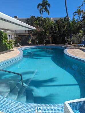 A clear blue pool with a 3.5 ft depth marker, surrounded by palm trees and a covered area.