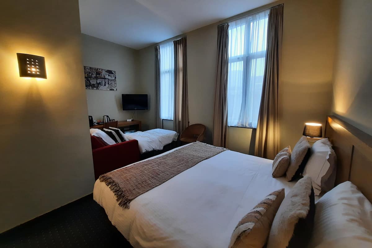Habitación de hotel con una cama grande, un escritorio con silla, televisión y ventana con cortinas.