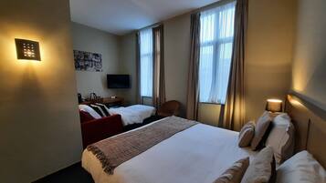 Ein Hotelzimmer mit einem großen Bett, einem Schreibtisch mit Stuhl, einem Fernseher und einem Fenster mit Vorhängen.