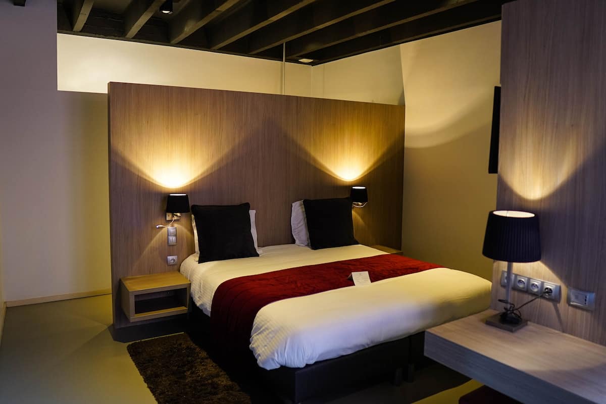 Una habitación de hotel moderna con una cama, lámparas de noche, una mesita de noche y un escritorio con lámpara.