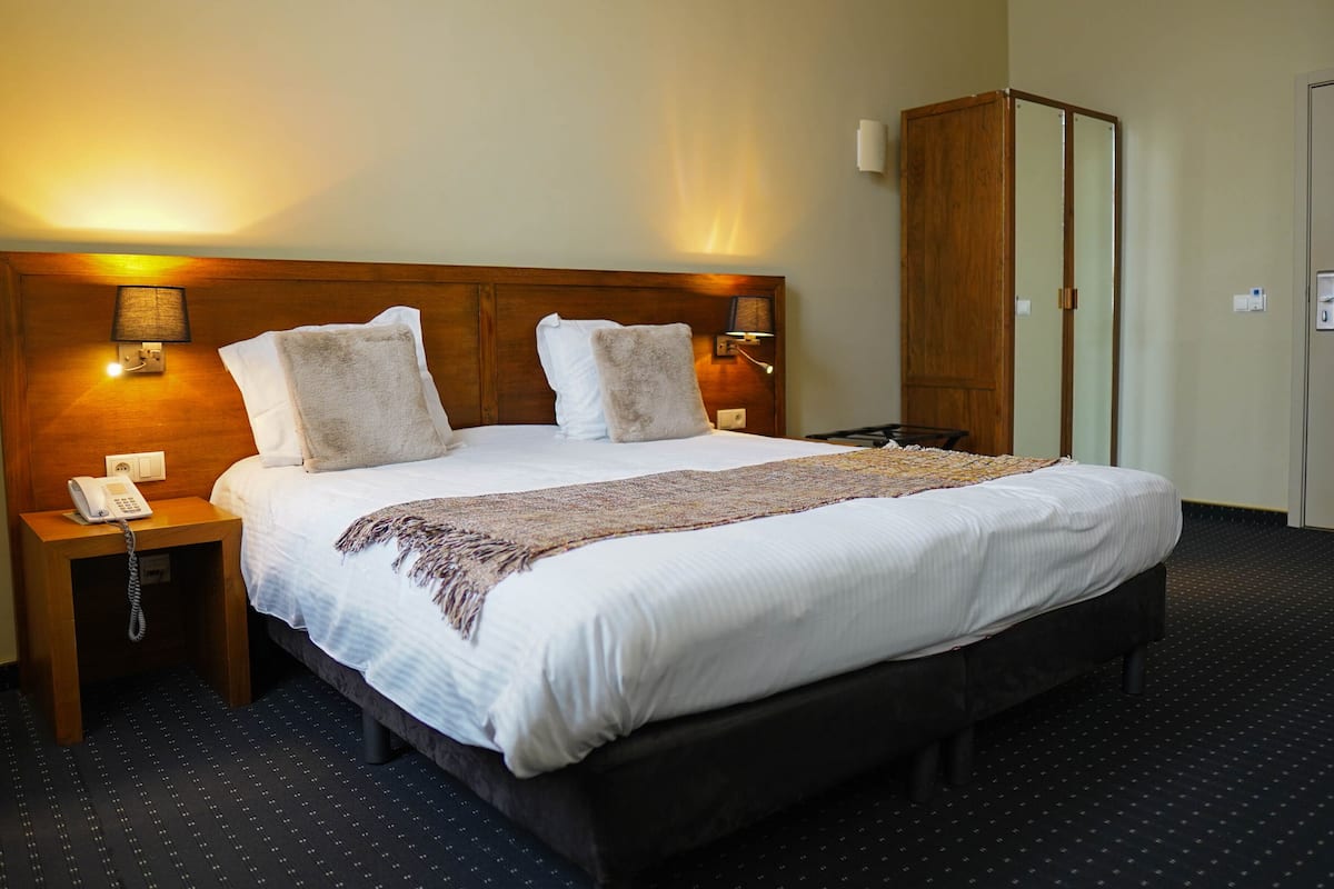 Una habitación de hotel con una cama grande, dos lámparas de noche, un teléfono y un armario.