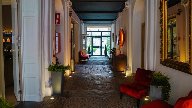 Un hall d’hôtel avec un sol à motifs en chevrons, des fauteuils rouges et un grand miroir sur le mur de droite.