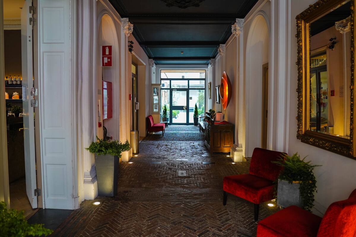 Un vestíbulo de hotel con suelo de diseño tablero de espiga, sillas tapizadas en rojo y un espejo grande en la pared derecha.