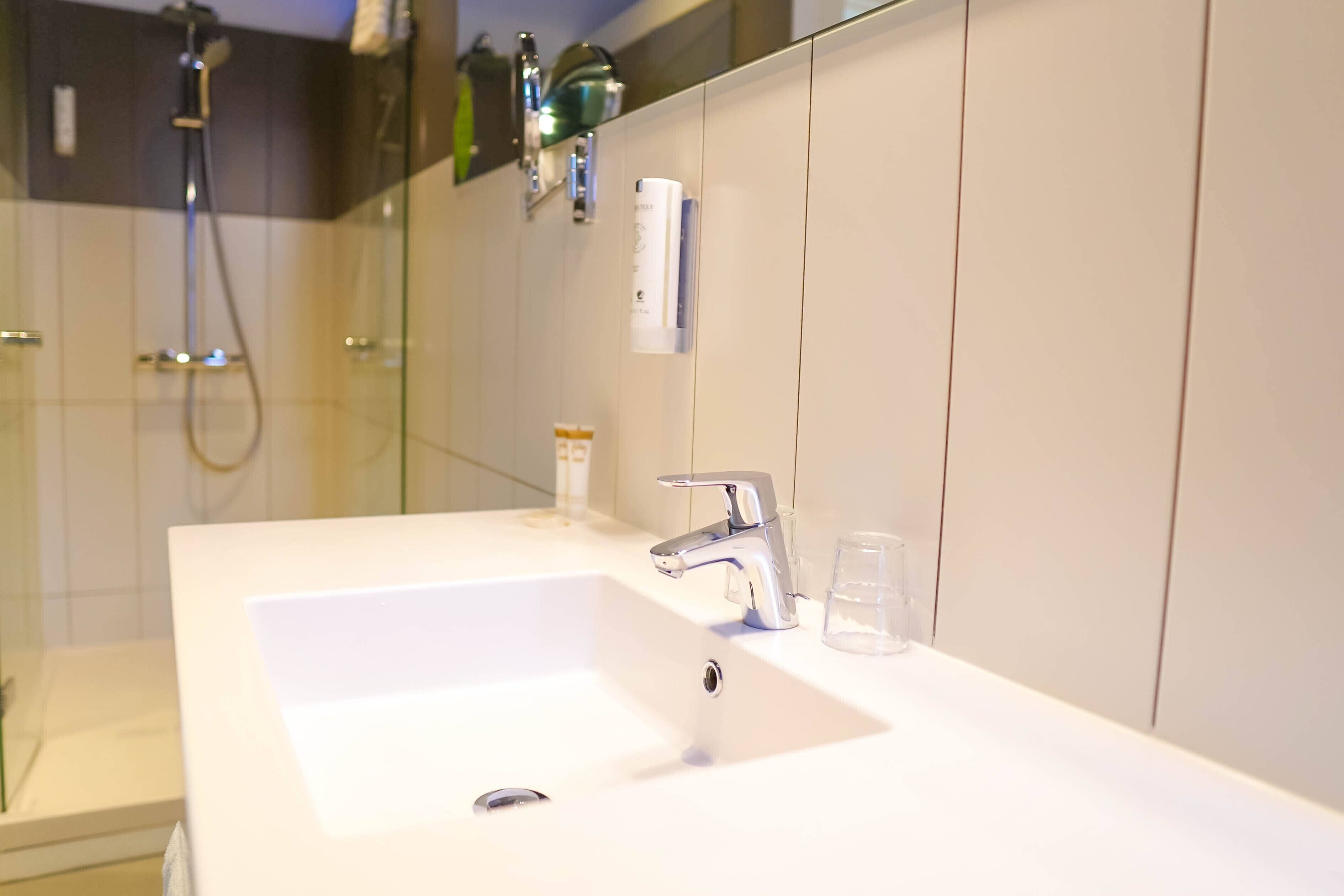 Une salle de bain avec un lavabo blanc, un robinet moderne et une douche à parois de verre.