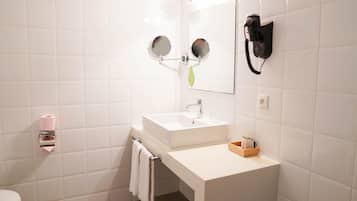 Une salle de bain avec des carreaux blancs, un lavabo, un miroir, un sèche-cheveux et des toilettes.
