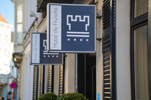 Une enseigne d’hôtel ornée d’une couronne et d’étoiles, indiquant qu’il s’agit de l’hôtel « Hôtel de Flandre ».