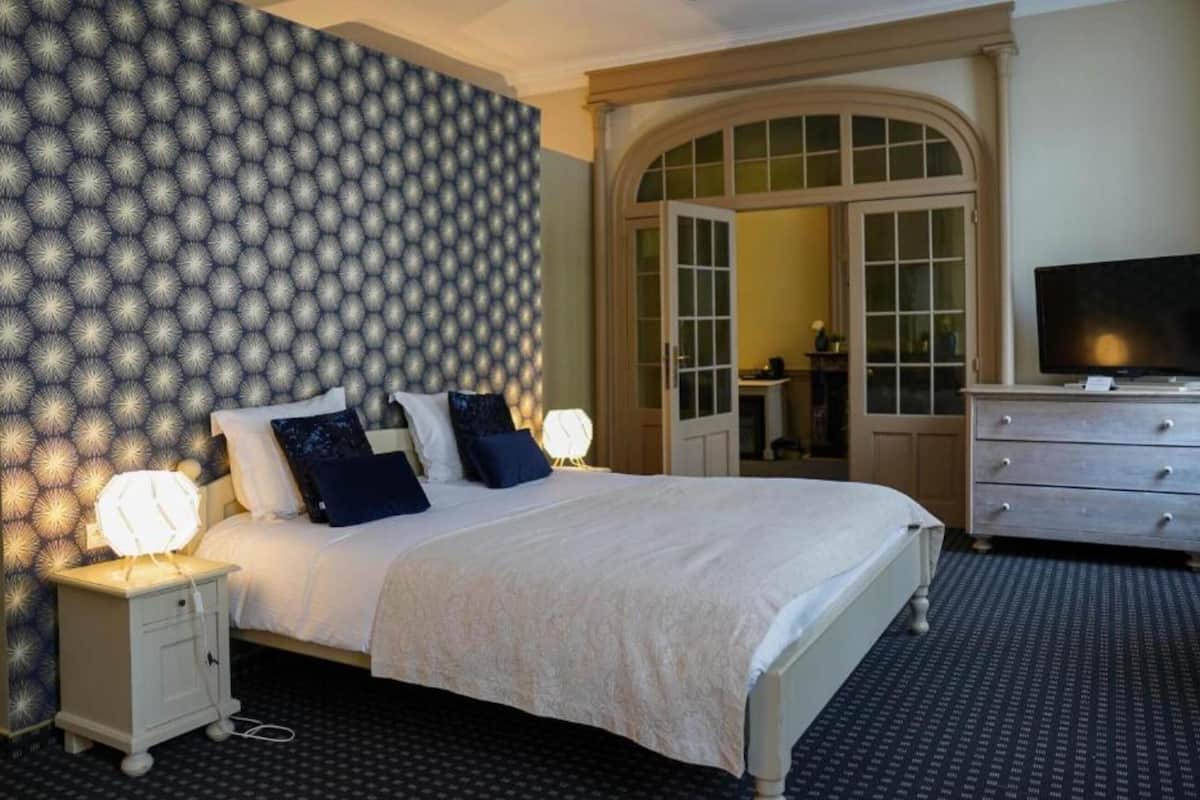 Una habitación de hotel con una cama grande, un aparador, un televisor y un papel tapiz estampado.