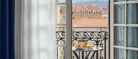 A balcony with a table, a bed, and a view of buildings.
