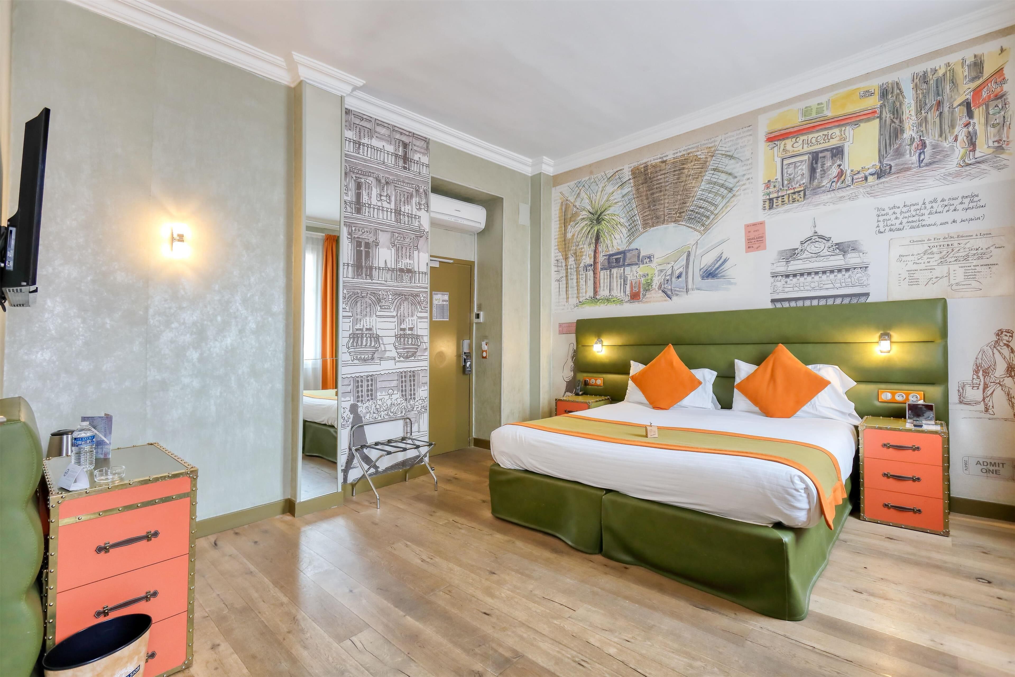 A hotel room with a green upholstered bed, orange pillows, a small side table, a green chair, a pink storage unit, and a wall with various illustrations and text.