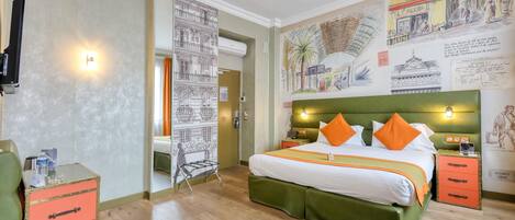 A hotel room with a green upholstered bed, orange pillows, a small side table, a green chair, a pink storage unit, and a wall with various illustrations and text.