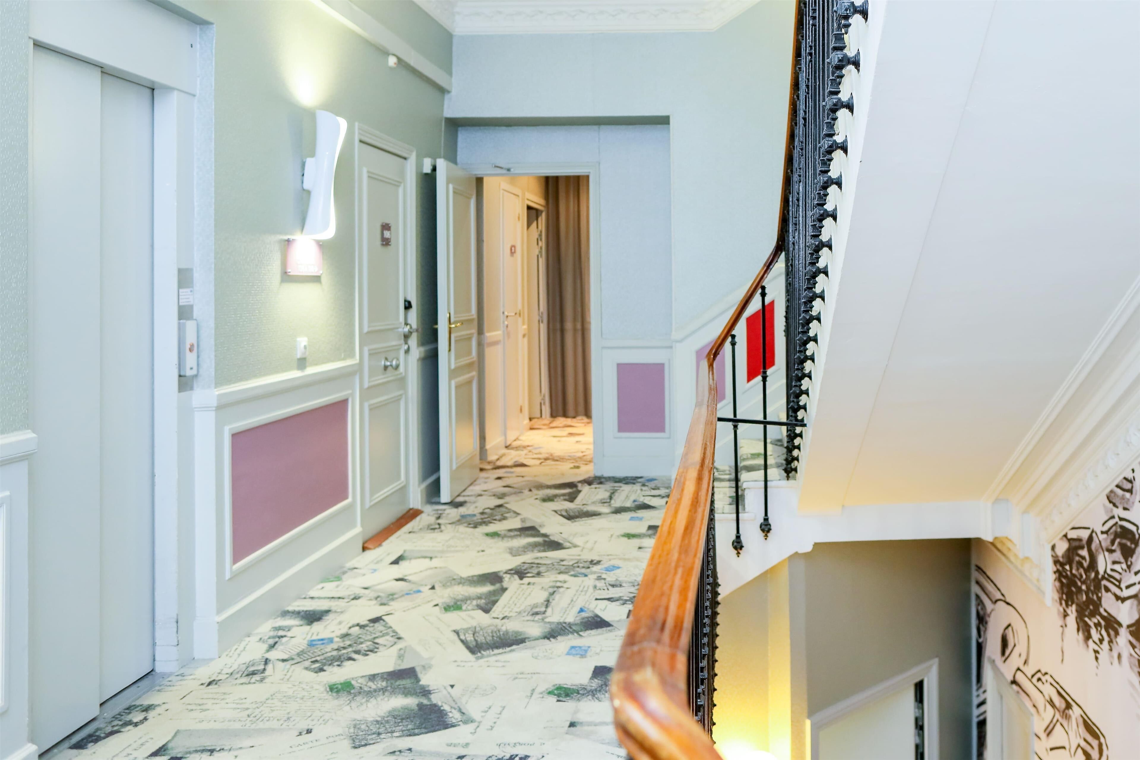 A hallway with a patterned floor, a staircase with a wooden handrail, and a wall-mounted light fixture.