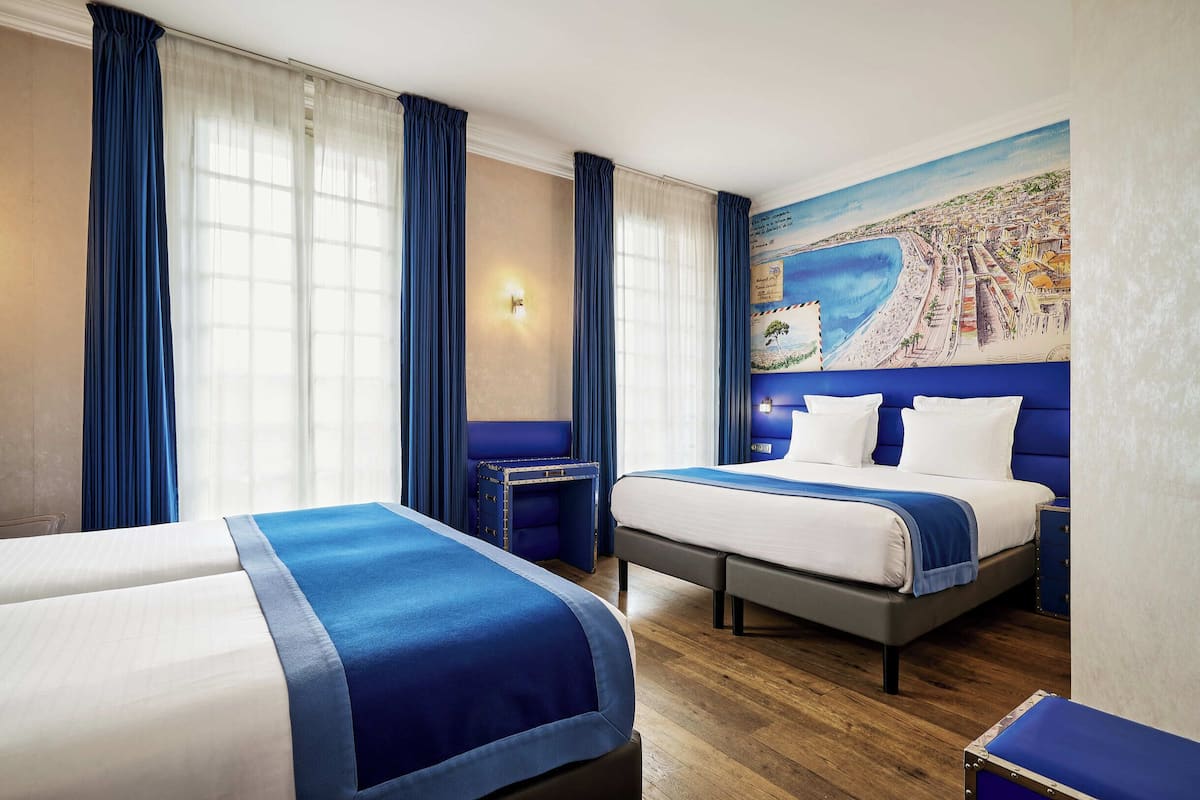 Hotellihuone, jossa on kaksi sänkyä, seinämaalaus, jossa on kuvattuna rannikkokaupunki, ja puulattia.