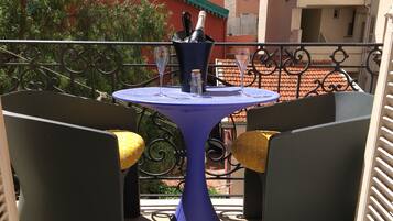 Un balcón con una mesa azul, dos sillas con cojines amarillos y una botella de champán.