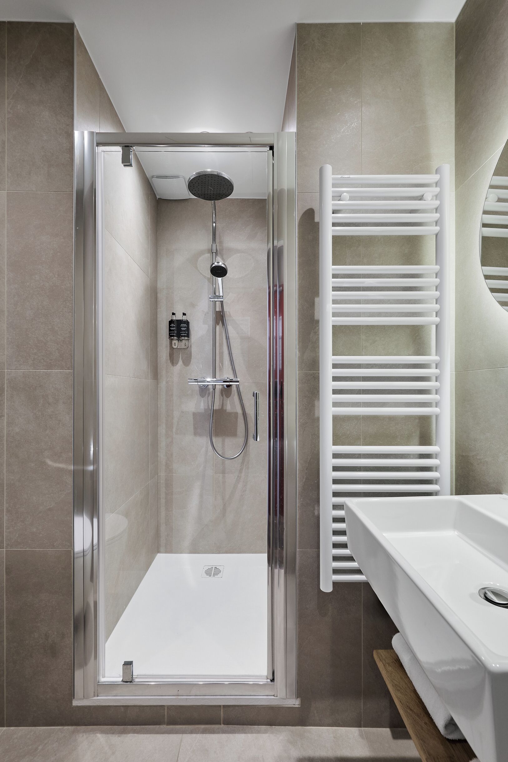 A modern shower enclosure with a glass door, a white towel rack, and a white sink with a wooden countertop.