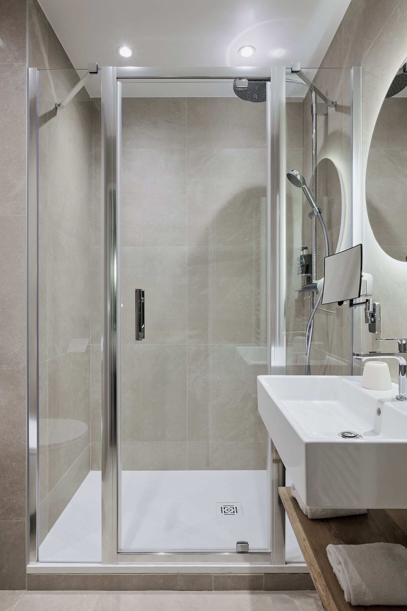 A modern bathroom with a glass-enclosed shower, a white sink, and a wooden vanity.