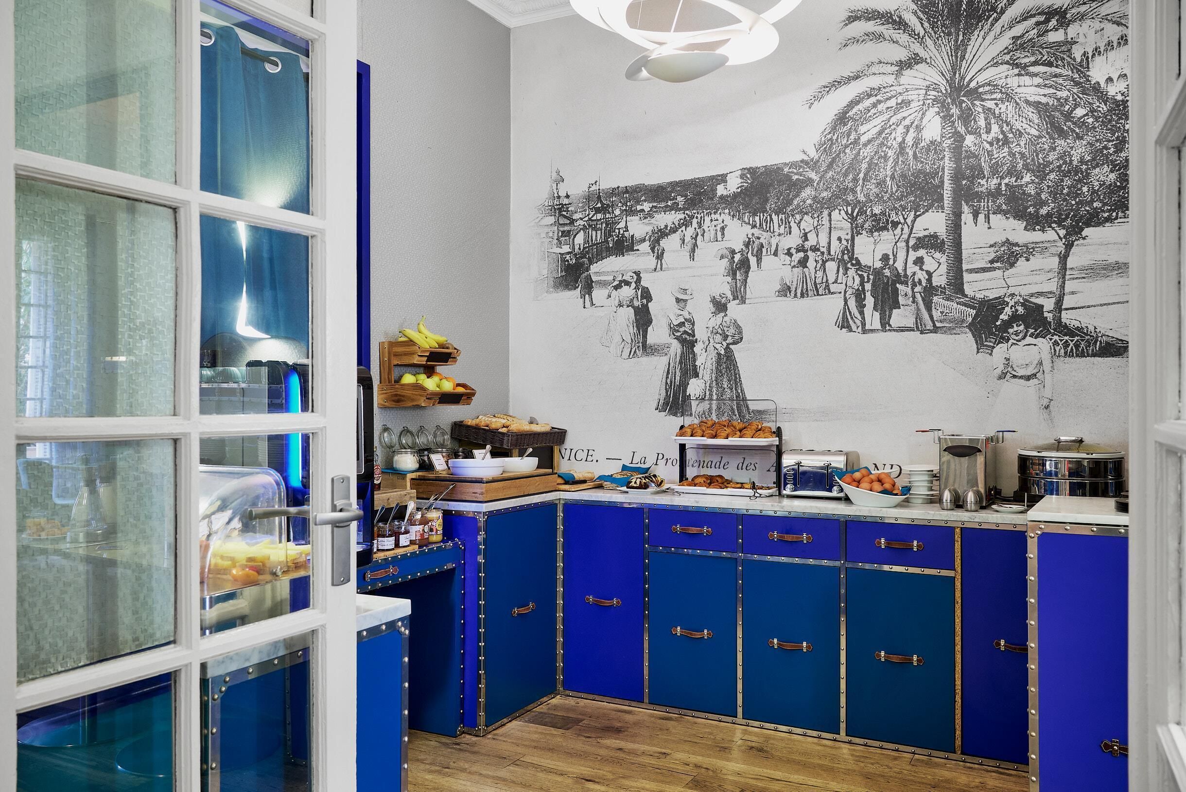 A kitchen with blue cabinets, a mural of a historical scene, and various kitchen appliances.