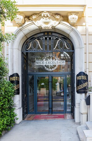 The entrance to the Nice Excelsior Hotel with a classic design, featuring a large arched doorway and a sign above the entrance. - Hôtel Excelsior by HappyCulture (Nice)